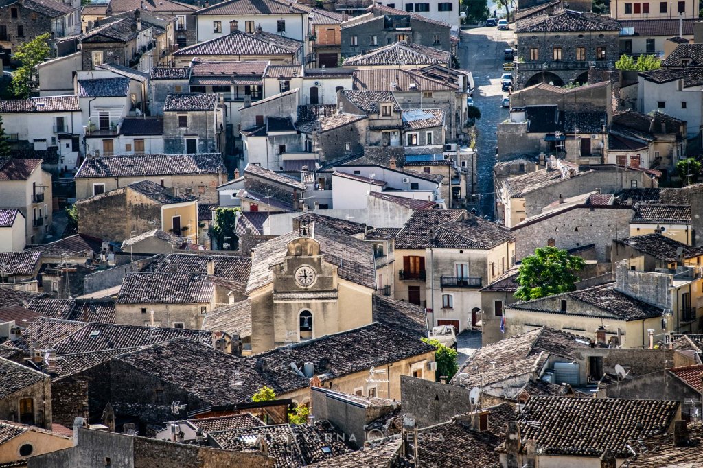 Aerial view of a small town with densely packed rooftops and a prominent clock tower in the center, surrounded by various buildings and greenery.