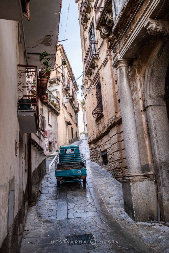 Narrow cobblestone street with a steep incline, lined with old buildings and a small blue truck parked on the side.